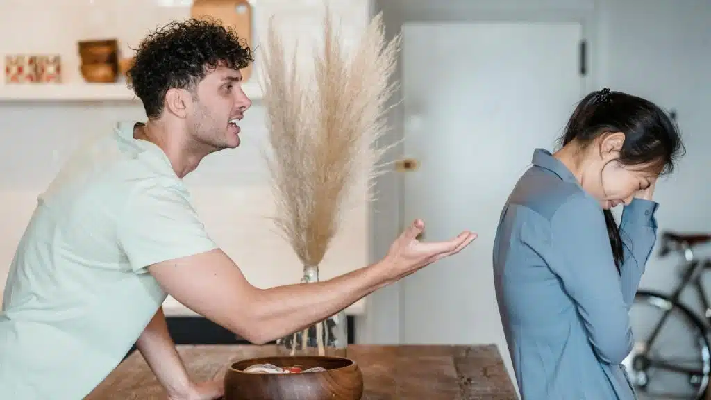 A man gestures with an open hand toward a woman who is looking down and crying.