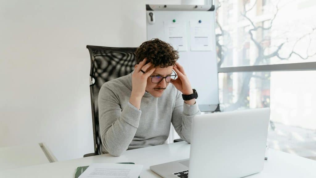 A man looking stressed while working on a laptop.