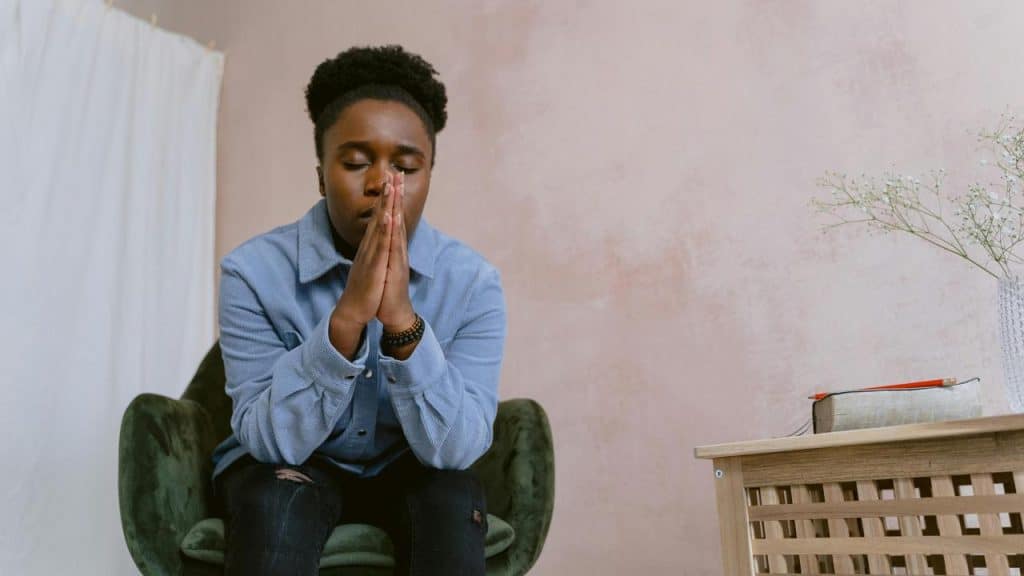 A person sits with their hands together, appearing to pray or reflect.