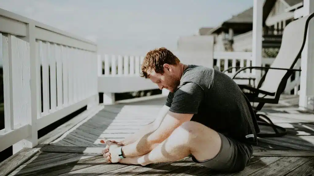 A man stretching on a wooden deck in daylight.