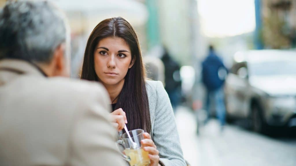 A woman with long dark hair looks seriously at a person during a meal outdoors.