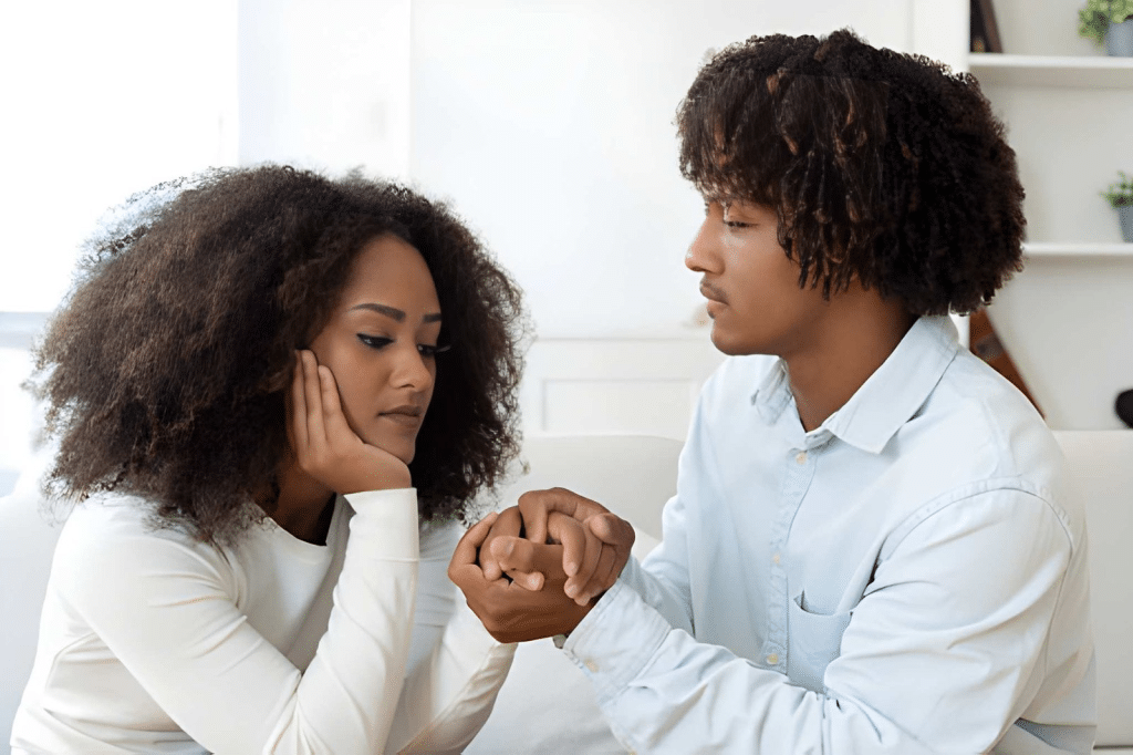 Sad young couple sitting on couch and holding hands