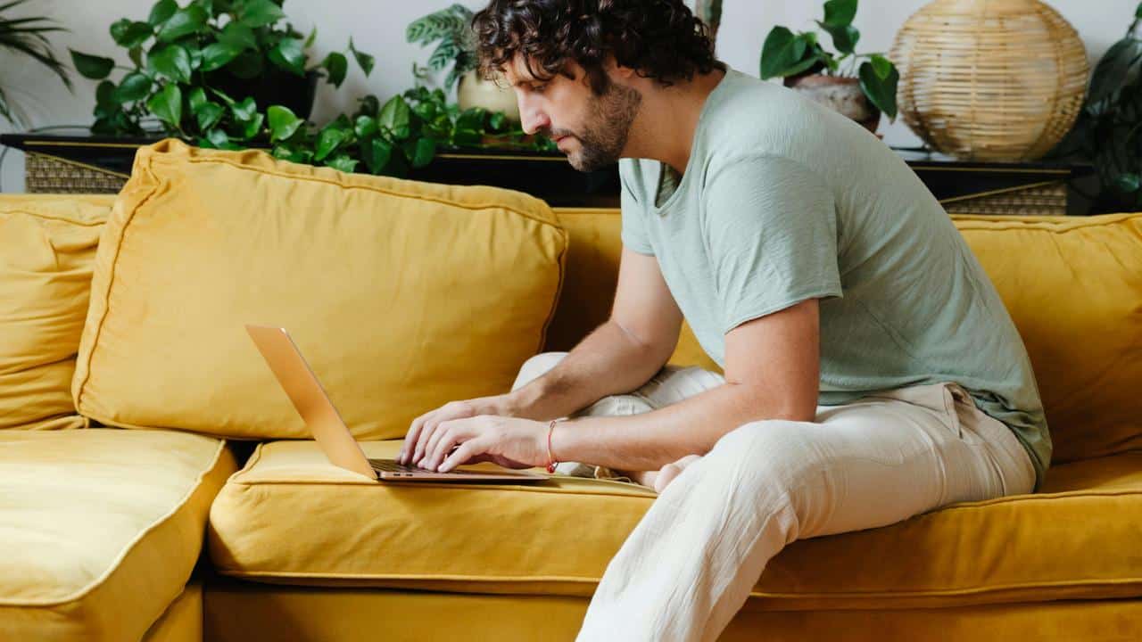 A man sitting on a yellow couch using a laptop.