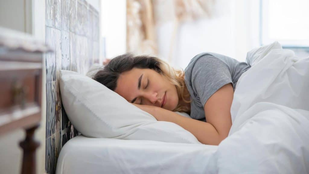 A woman sleeping peacefully in bed with white sheets.