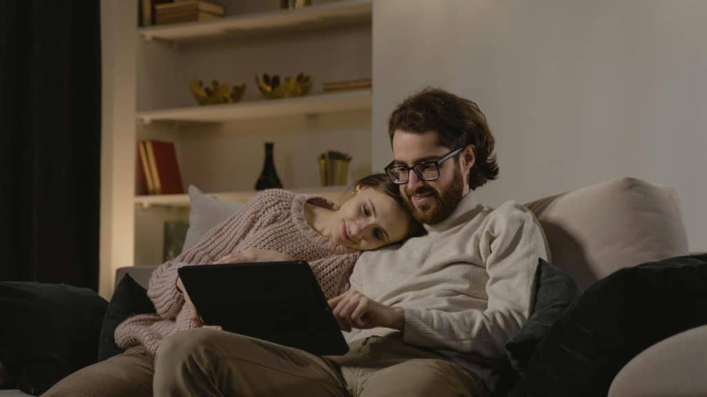 A couple sitting on a couch watching a tablet together