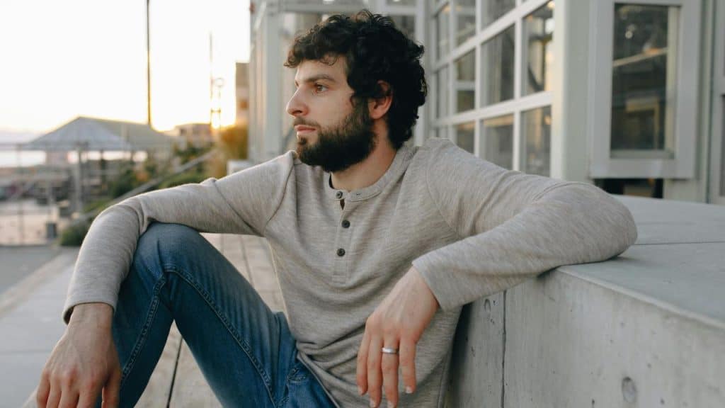 A man sitting outdoors near a building, looking into the distance.