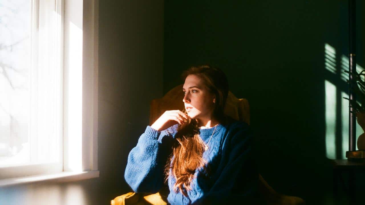 A woman sitting by a window looking thoughtful.
