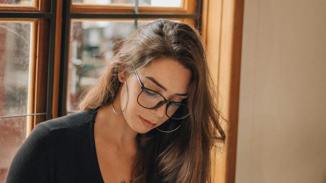 A woman wearing glasses looking down indoors.