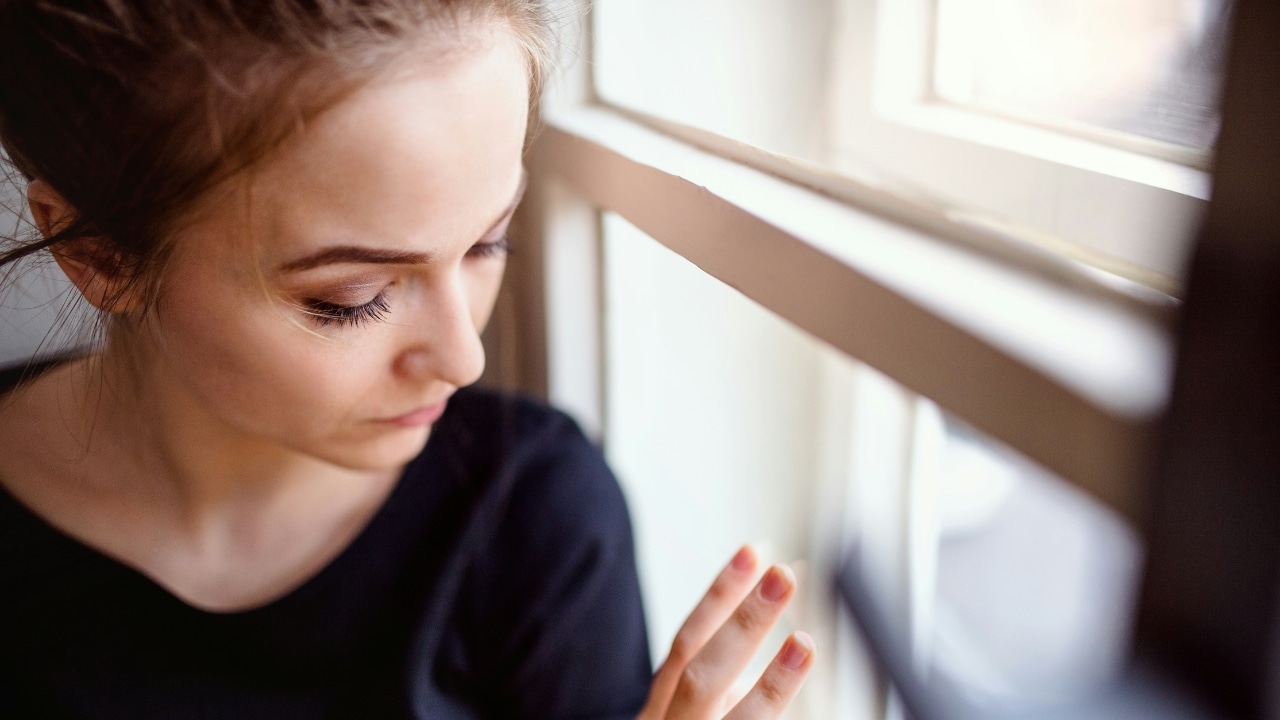 A close-up, high-angle view of a woman looking down while resting her hand on a window.