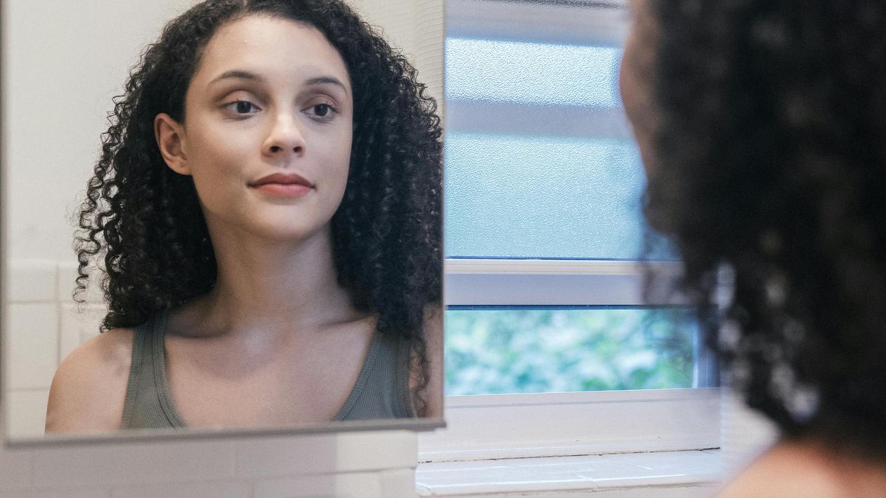 A woman looking at herself in a mirror with a calm expression.