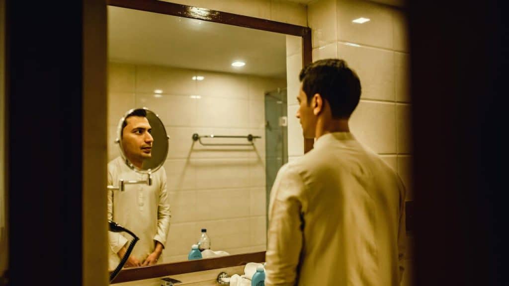 A man looking at his reflection in a bathroom mirror.