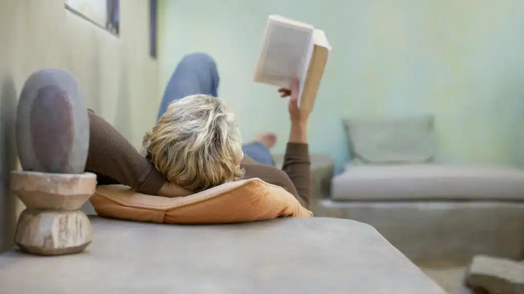 A person lying on a sofa and reading a book in a calm, minimalist room.
