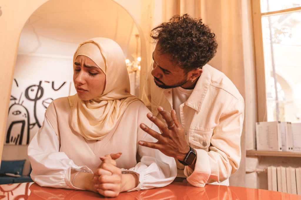 A furious man is talking to a man with an unhappy woman in hijab.