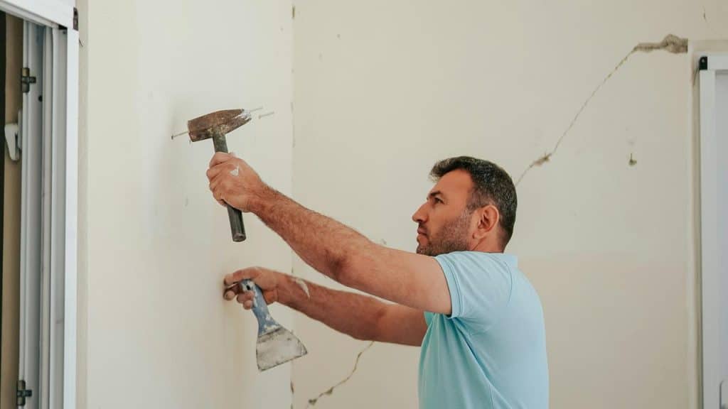 A man repairing a wall with a hammer and scraper.