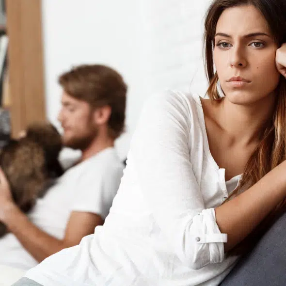 Disappointed woman on couch with man and pet in background
