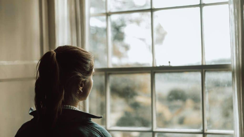 A woman standing by a window looking outside.