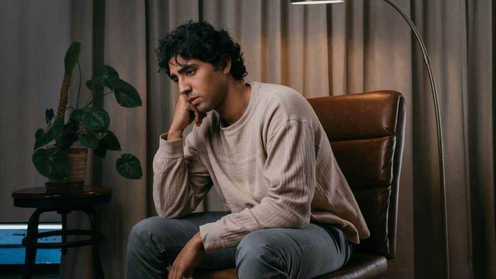 A man sits in a leather chair with his chin resting on his hand, looking away.