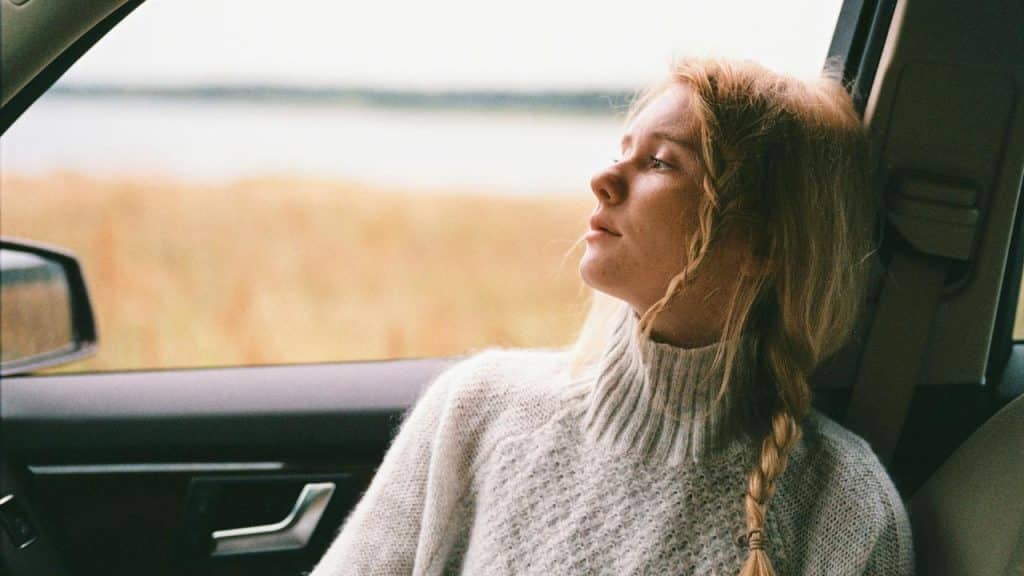 A woman sitting in a car looking out the window thoughtfully.