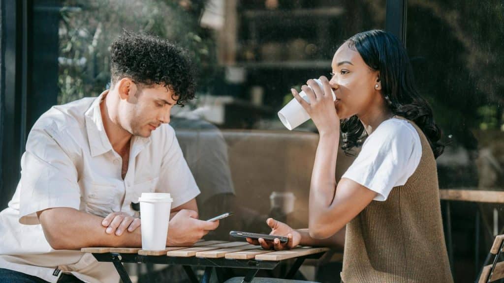 A man and woman sitting at an outdoor café table with coffee cups and phones.