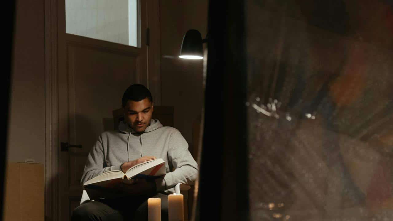 A person sitting indoors reading a book by candlelight.