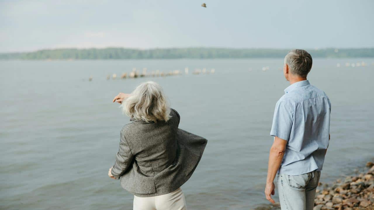 A senior couple standing by the water, watching the waves.