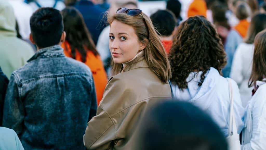 A woman with sunglasses on her head looks back while standing in a large crowd.