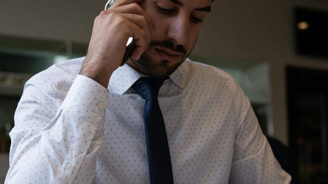 A man in a dress shirt and tie talking on a phone while looking down.