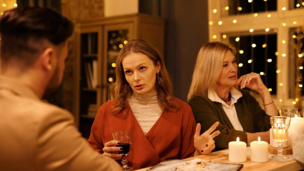 Two women and a man sit at a candlelit table; one woman is gesturing while speaking.