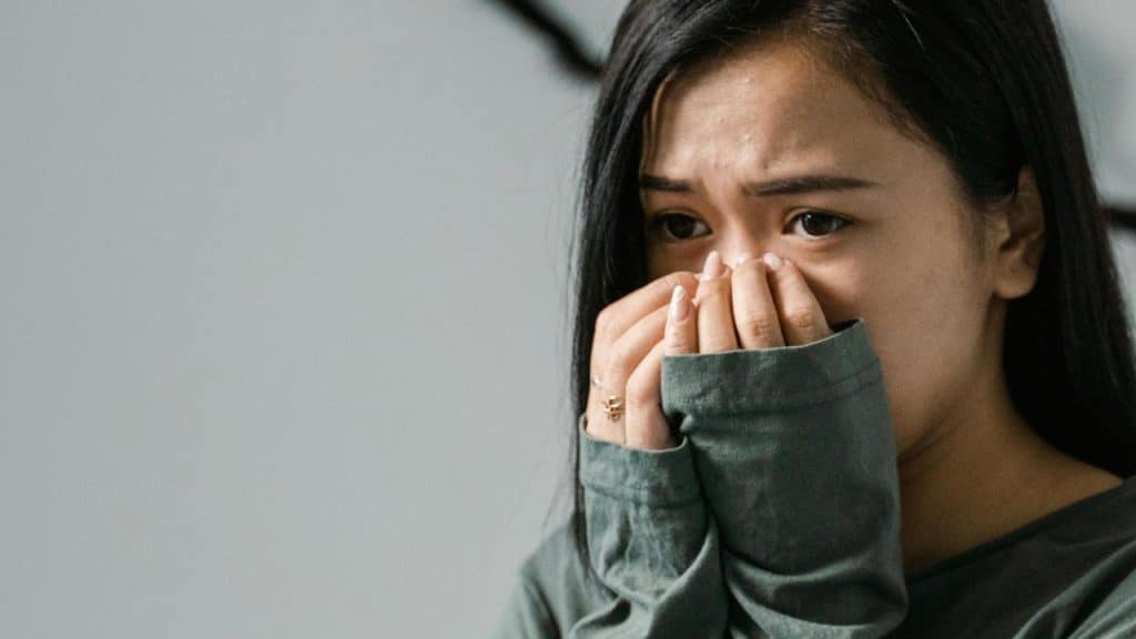 A woman covering her nose and mouth with her hands, looking worried.