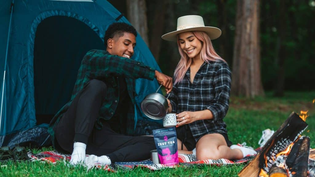 A man and woman sitting on a blanket next to a tent.