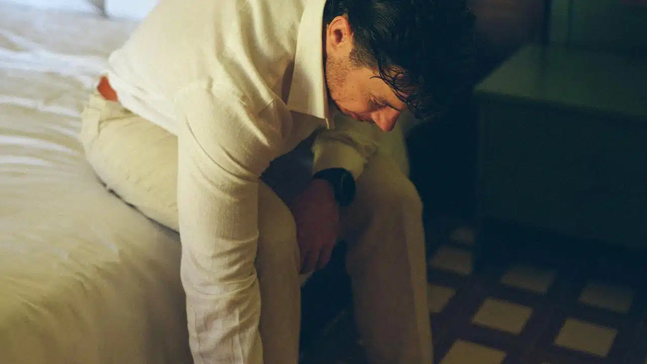 A man sitting on a bed with his head lowered.