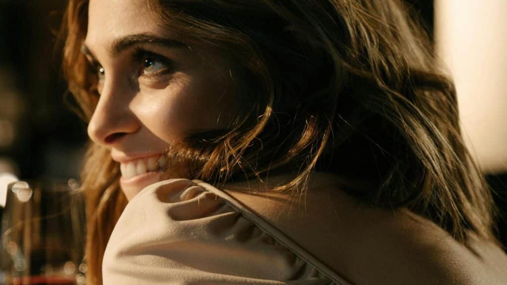 A woman smiling and looking to the side in warm lighting.