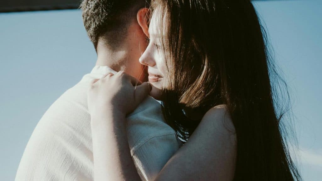 A couple embracing closely, with the woman resting her head on the man’s shoulder.