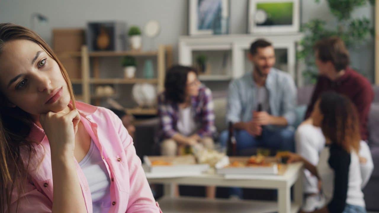 A woman in a pink shirt looks forward while people sit blurred in the background.