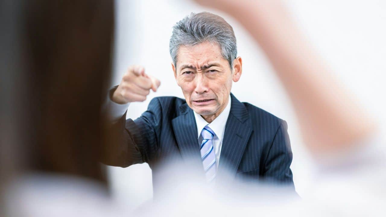 A man in a suit looks toward a woman who is gesturing with her hand.
