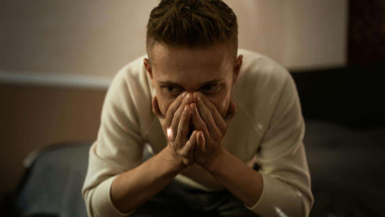 A man leaning forward with his hands covering his mouth, looking anxious.