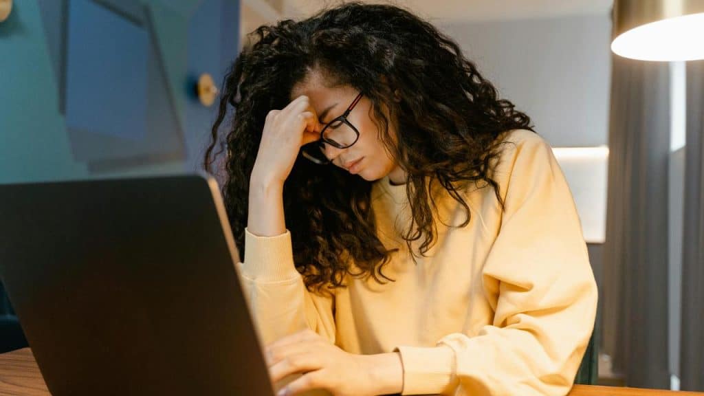 A woman wearing glasses looks stressed while working on a laptop.