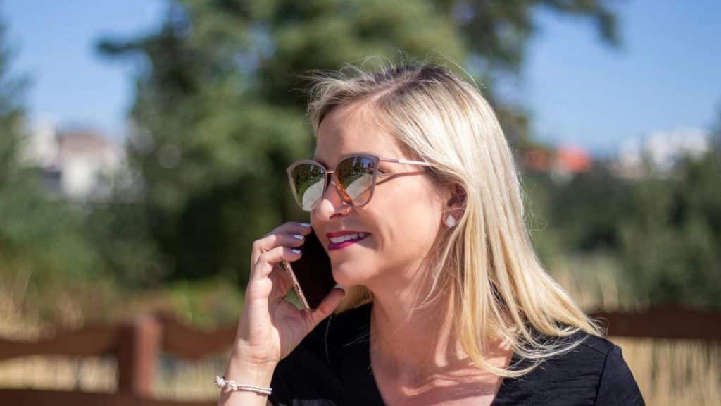 A woman wearing sunglasses talking on the phone outdoors.