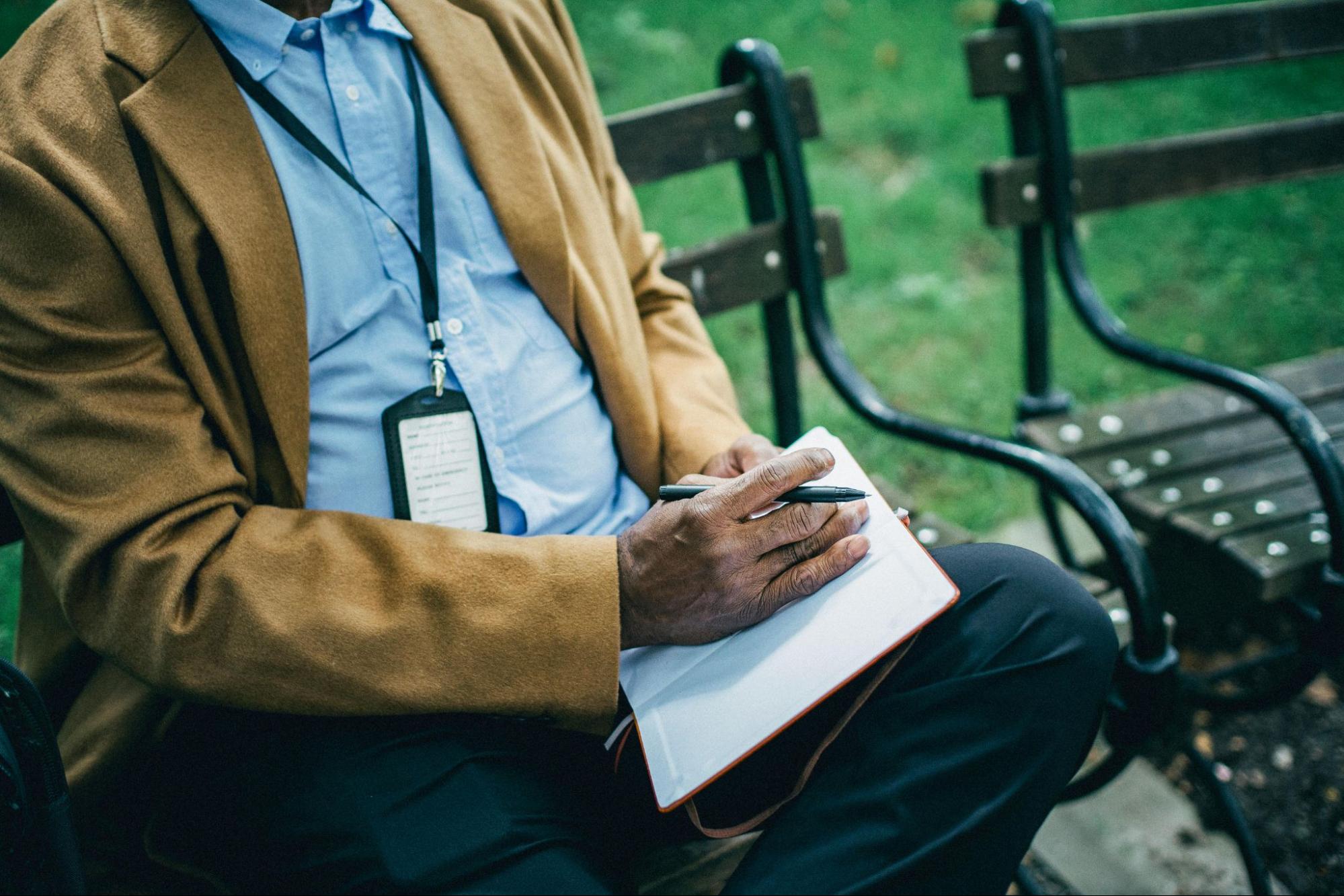 A man writing on a notebook outside.