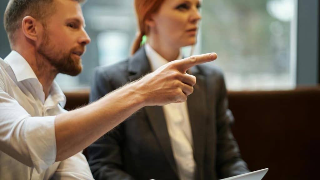 A man pointing while talking with a woman in a meeting.
