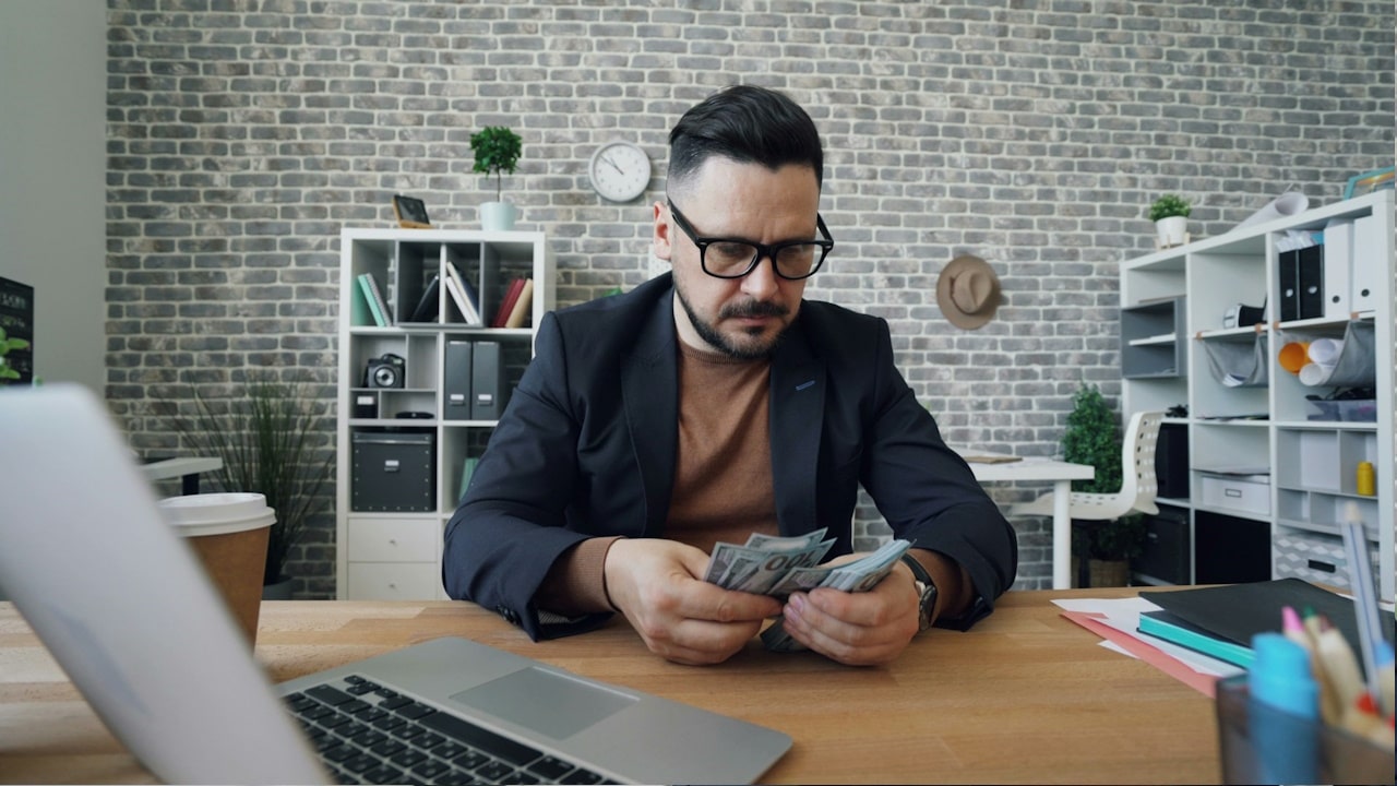 A man sitting at a table with a laptop and money.