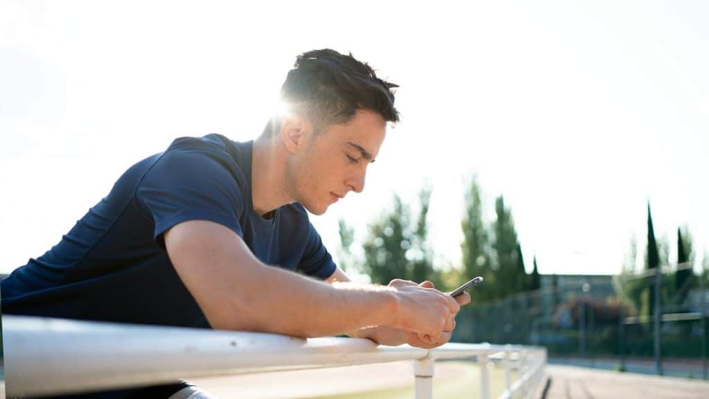 A man leaning on a railing outdoors while using his smartphone.