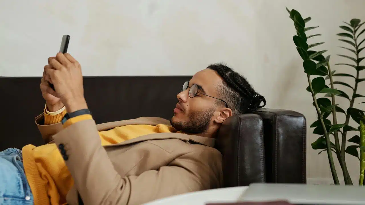 A man reclining on a couch and looking at his phone.