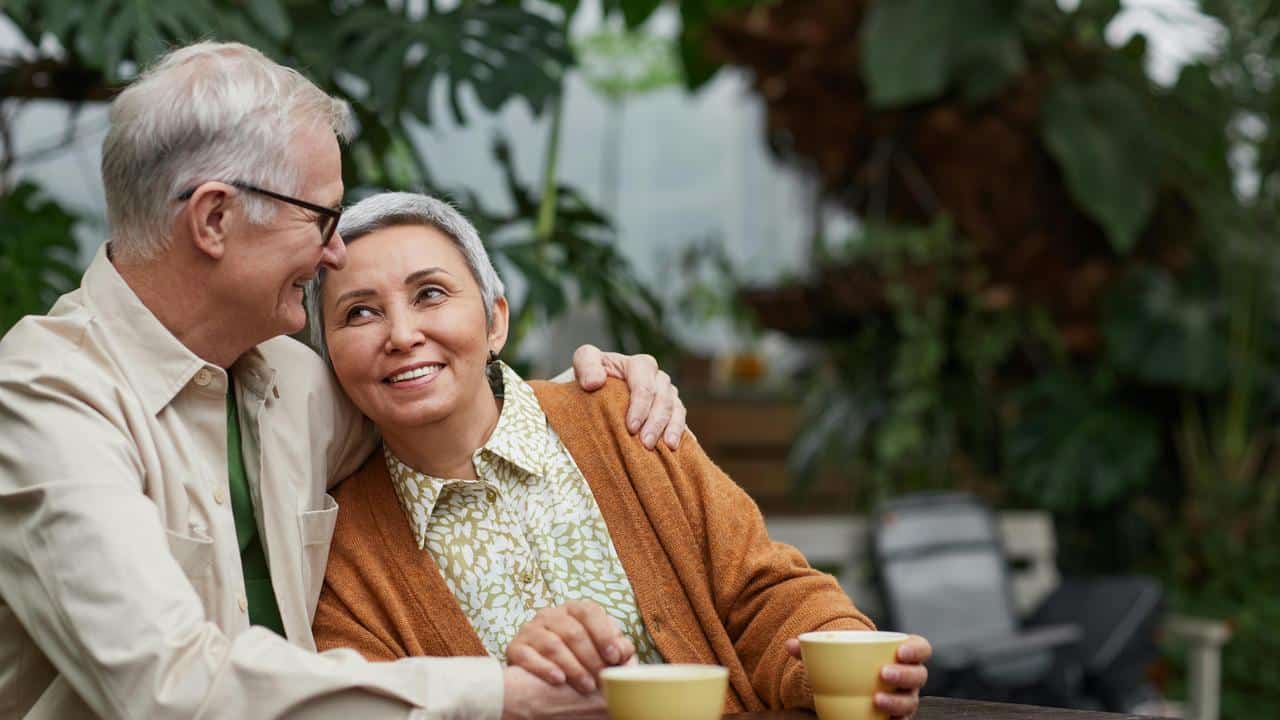 A senior couple sitting together at a table, smiling while enjoying drinks.