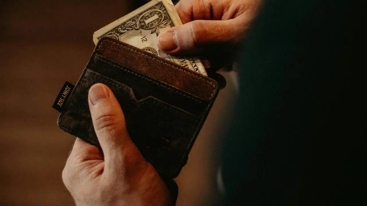 A person pulling a dollar bill from a worn leather wallet.