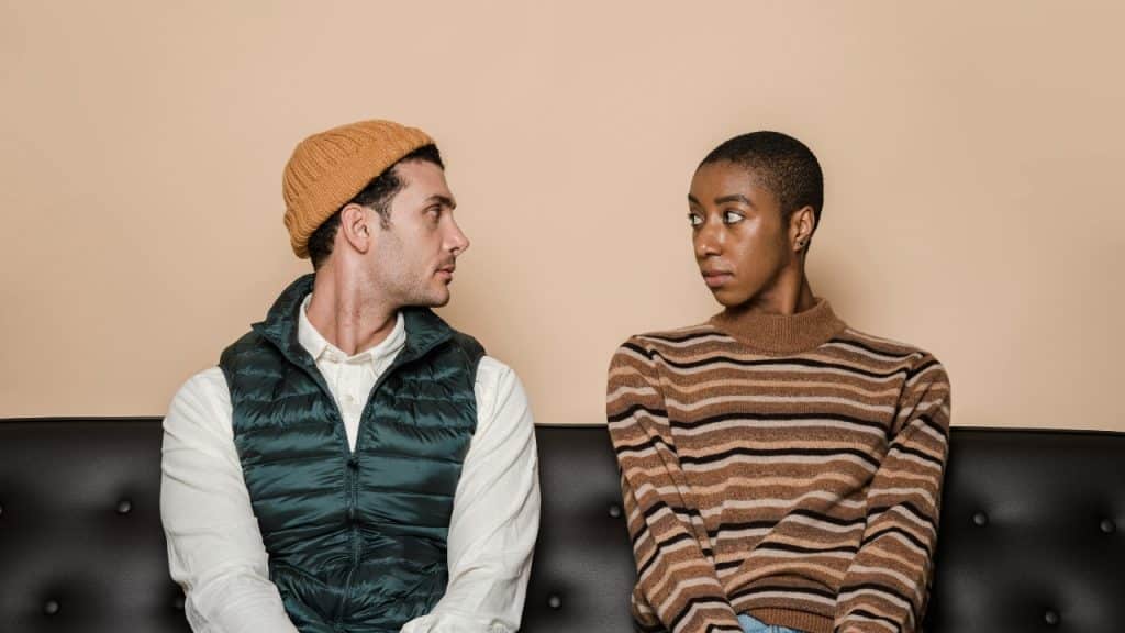 A man in a yellow beanie and a woman in a striped sweater look at each other.