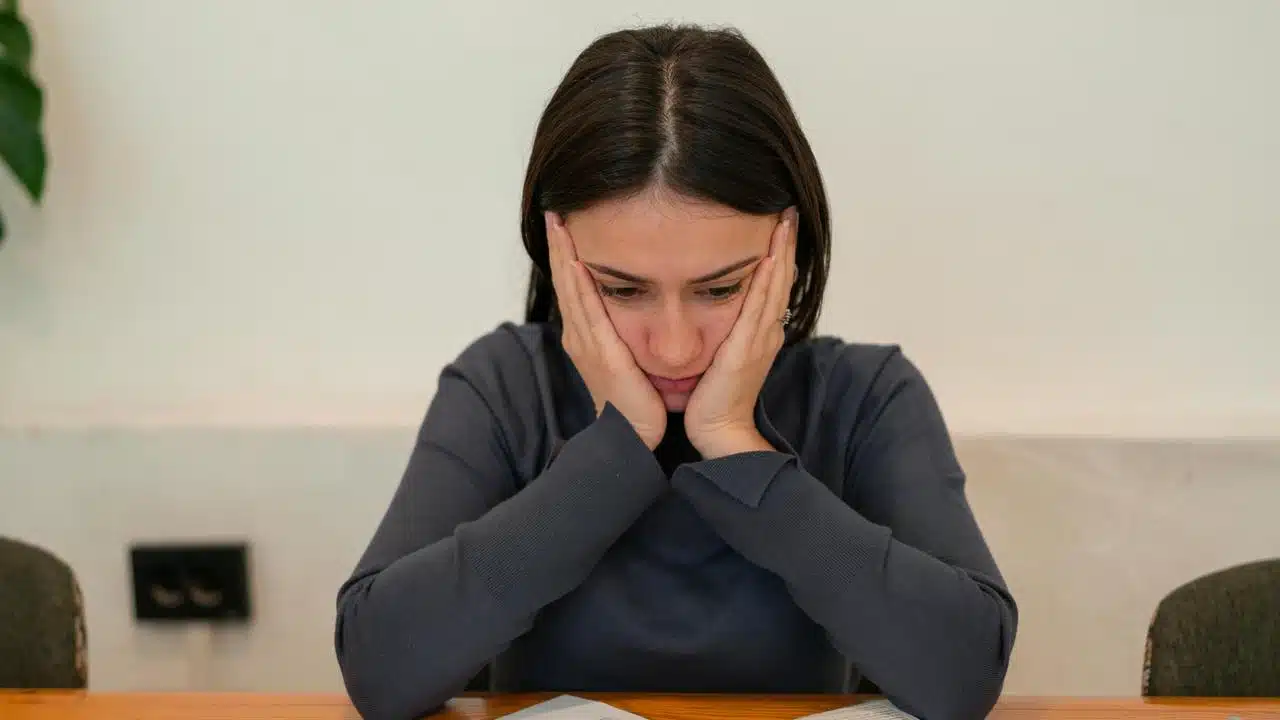 A woman holding her face while looking down at papers on a table.
