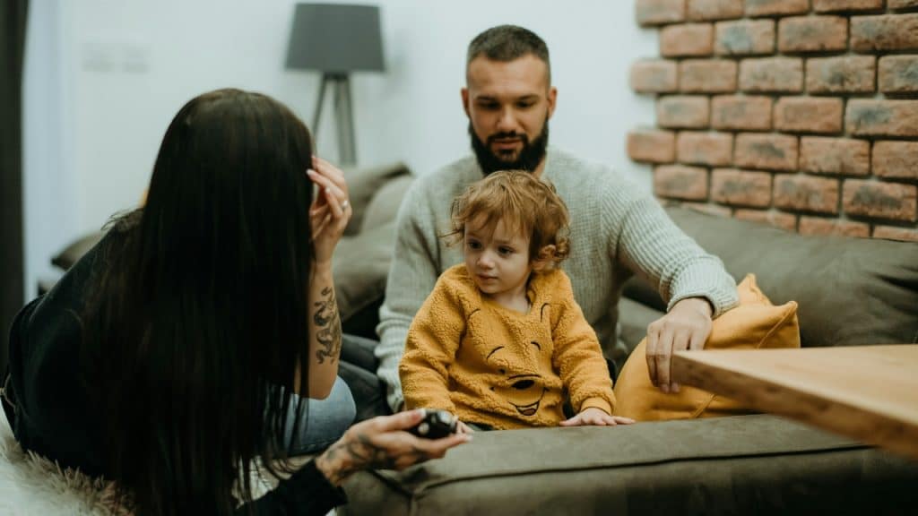 A man and woman sit on a sofa with a small child between them.