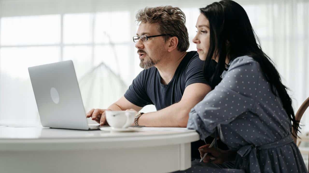 A man and woman focused on a laptop while sitting at a table with a cup of coffee.