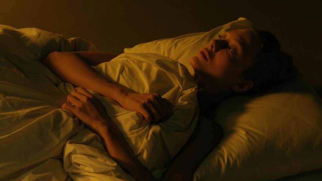 A person lying awake in bed under warm, dim lighting.